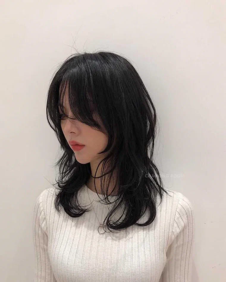 Cô gái tóc đen dài quá ngực, mái thưa dài phủ ngang mắt, ngọn tỉa vát bay nhẹ