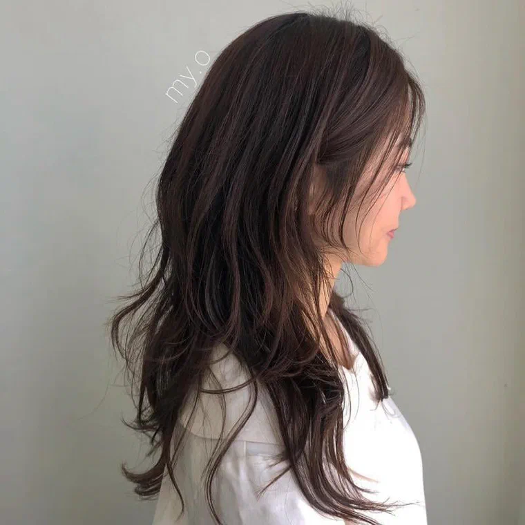 Cô gái tóc nâu nhìn nghiêng, các tầng phía sau uốn cụp và ngọn tỉa vát thành từng lọn