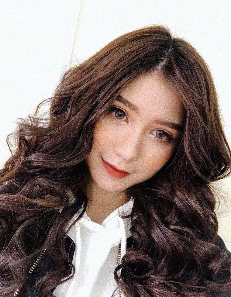An Japan tóc nâu socola dài quá ngực, uốn lọn to đều từ ngang cằm xuống, rẽ ngôi lệch, mặc áo hoodie trắng