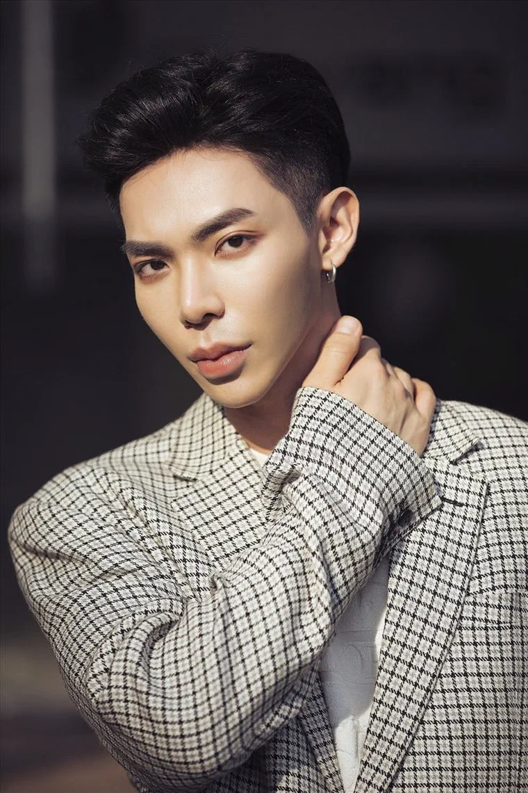 Erik mặc blazer kẻ caro, tóc đen vuốt ngược để lộ hết trán