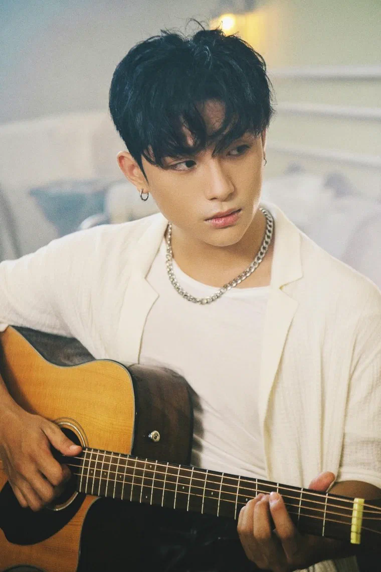 GREY D ôm đàn guitar, tóc đen với phần mái dày phủ kín trán xuống ngang chân mày, hai bên tỉa tầng che một phần tai