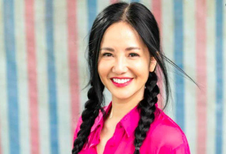 Hồng Nhung tóc đen rẽ ngôi giữa, tết hai bím ba lỏng thả trước vai, vài sợi tóc mai rơi trước trán, mặc sơ mi hồng
