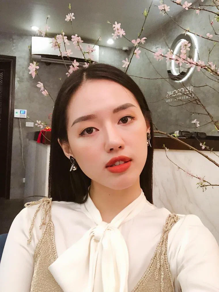 Khánh Linh tóc đen dài thẳng rẽ ngôi giữa, vén ra sau vai, môi đỏ cam