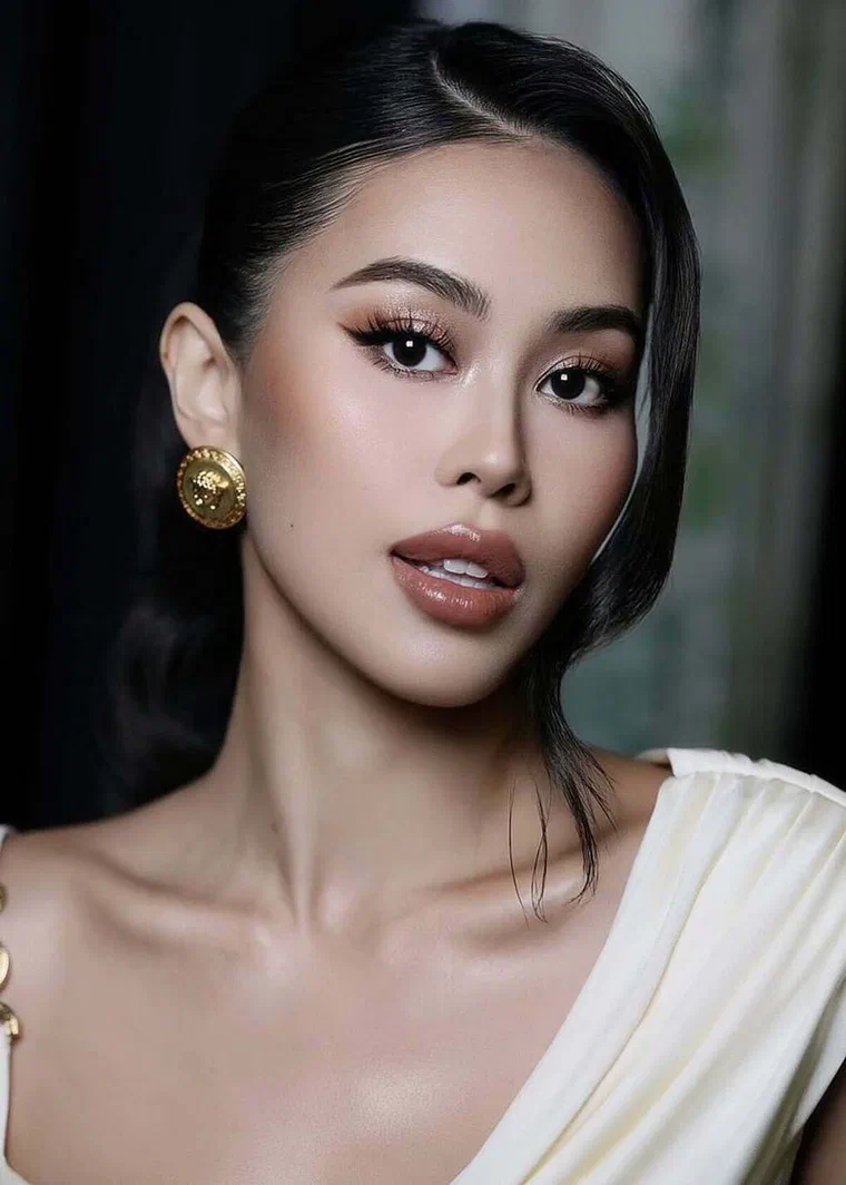 Tiên Nguyễn tóc đen rẽ ngôi lệch sâu, phần tóc trước vuốt bóng ôm sát đầu rồi gom gọn ra sau, khuyên tai vàng tròn