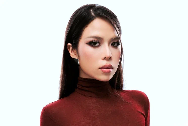 tlinh mặc áo cổ lọ đỏ, tóc đen dài rẽ ngôi giữa ép thẳng bóng, một bên vén hẳn ra sau tai