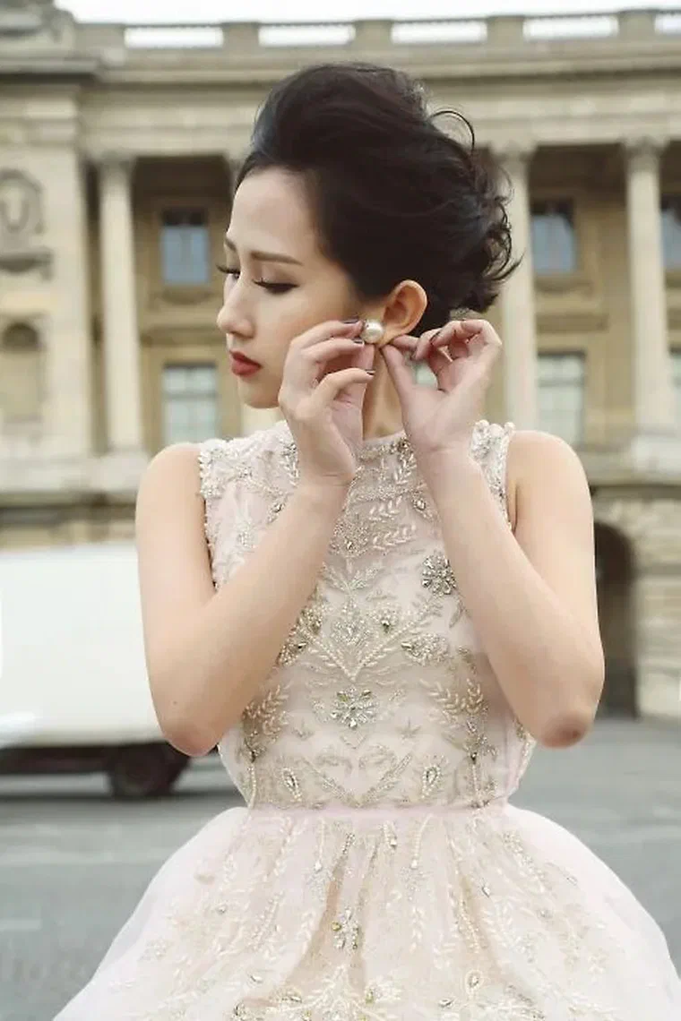 Trâm Nguyễn tóc đen búi cao phồng trên đỉnh đầu, vài lọn tóc con rủ xuống thái dương, nền kiến trúc Paris