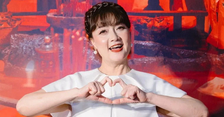 Vân Dung mặc áo trắng, tay tạo hình trái tim, tóc nâu vén ra sau tai, mái thưa, một bím tết chạy ngang đỉnh đầu như vương miện