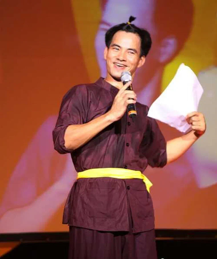 Xuân Bắc mặc áo nâu thắt lưng vàng, cầm micro, tóc hai bên ngắn, trên đỉnh có chỏm tóc nhỏ buộc dây vàng